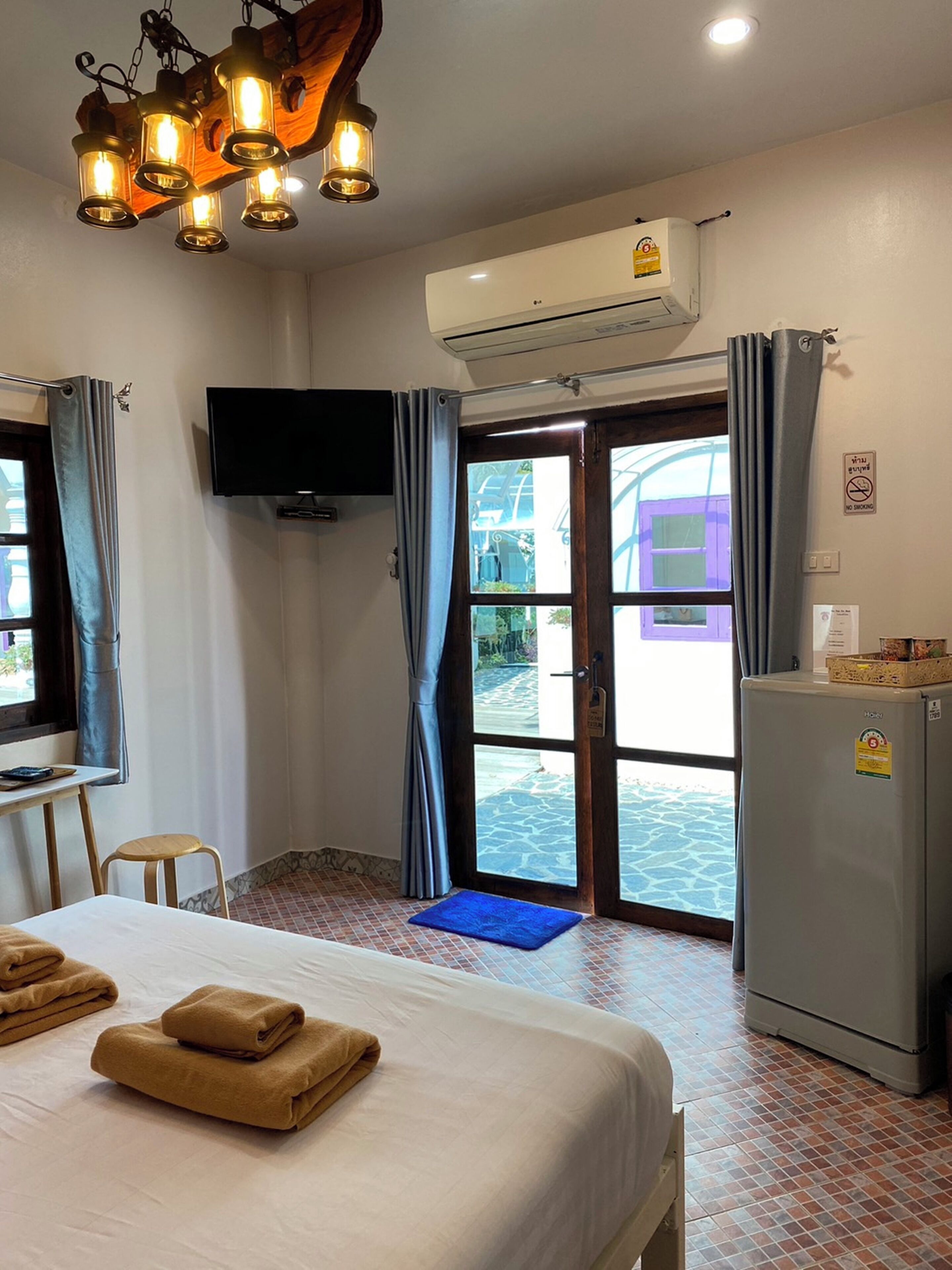 A hotel room with a bed, a desk, a television, an air conditioning unit, and a refrigerator.