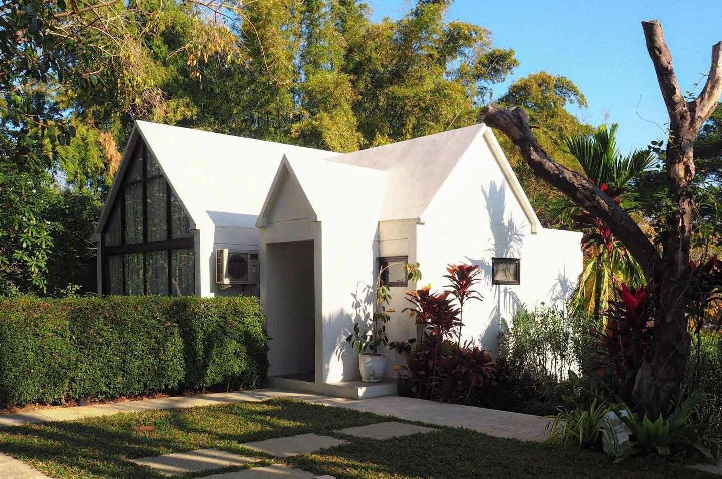 Een modern huis met een witte gevel, een groot raam en een verzorgde tuin.