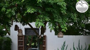 Un jardín con un sendero de piedra, una pared blanca con motivos vegetales y un coche aparcado al fondo.