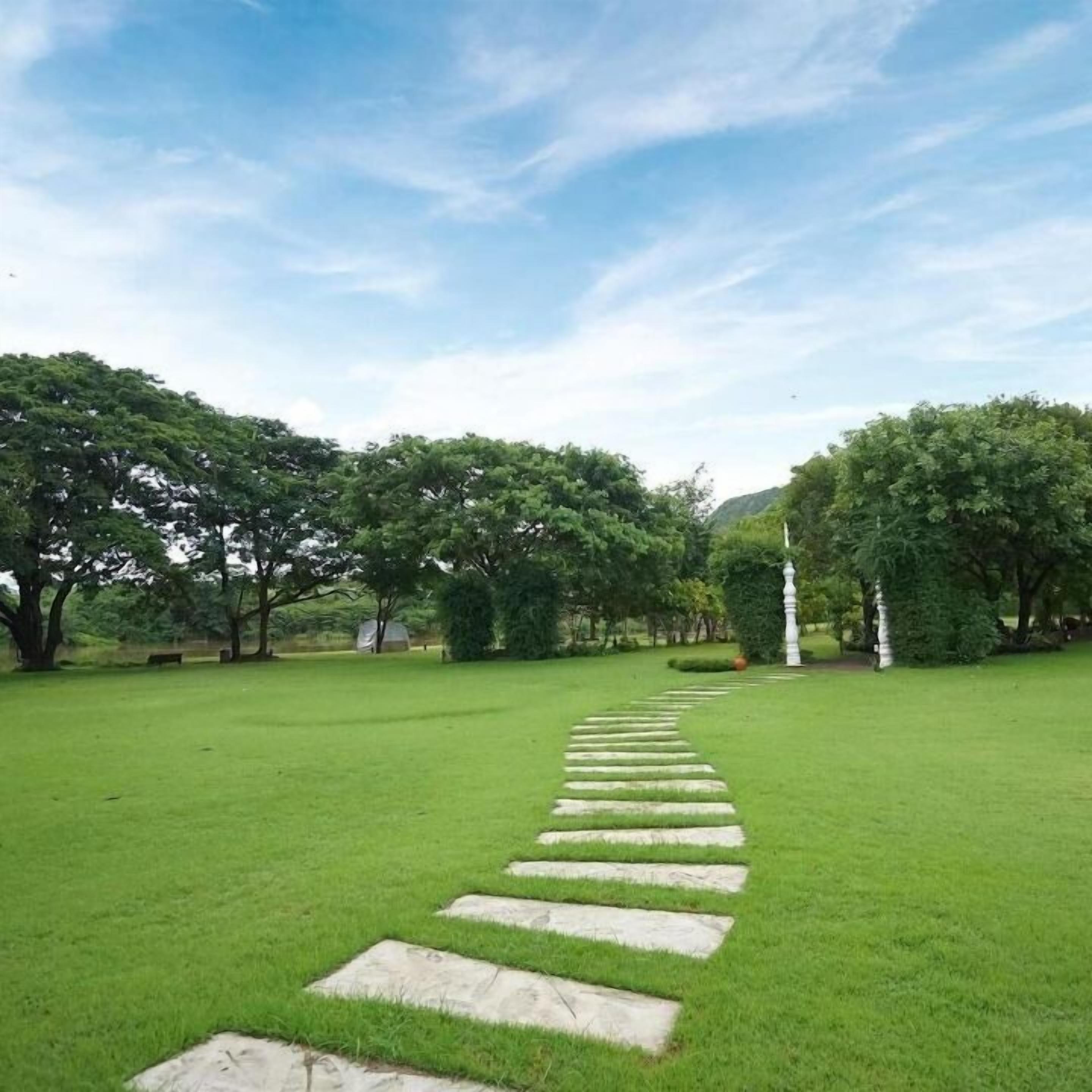 A pathway leading through a park with trees and a white statue.