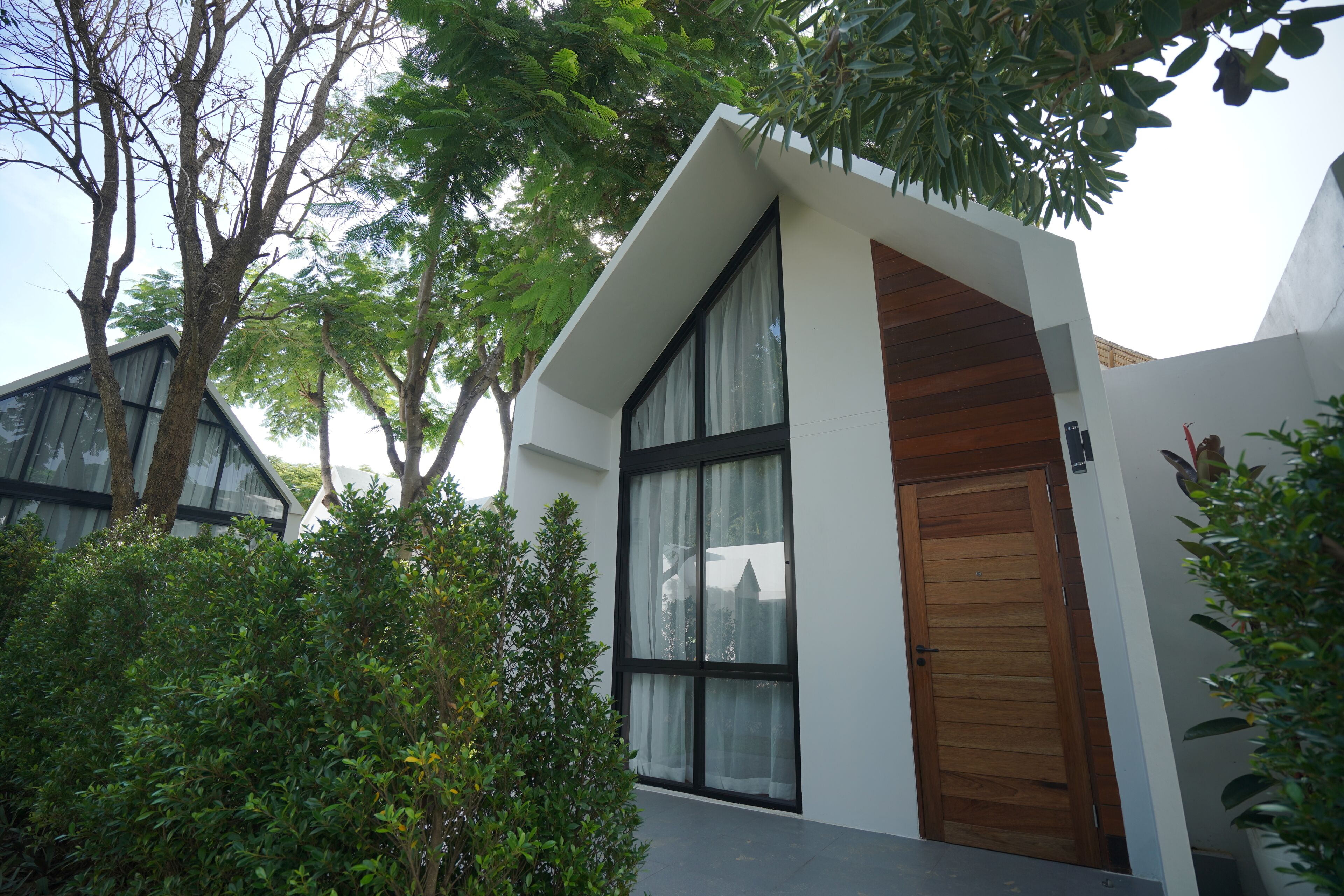 A modern building with large windows, a wooden door, and surrounding greenery.