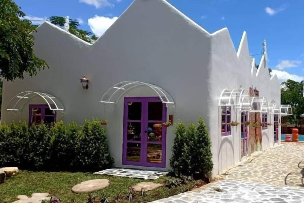 A white building with purple doors and windows, a paved pathway, and a small garden area.