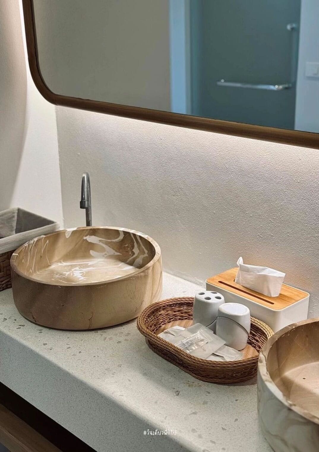 A bathroom with a wooden sink, a mirror, a small wooden box with tissues, and a wicker basket with toiletries.