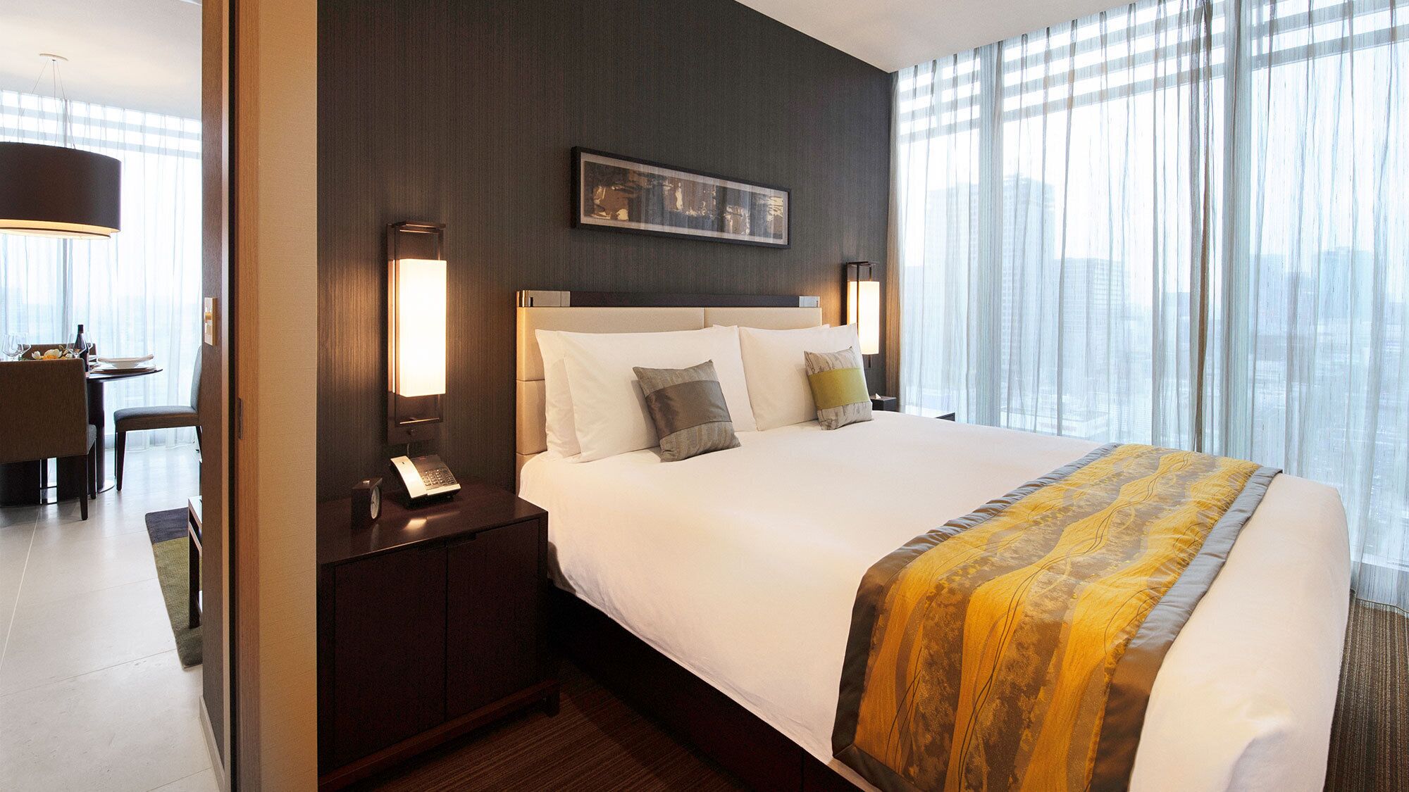 A hotel room with a large bed, a bedside table with a lamp, a clock, and a framed picture on the wall.
