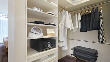 A hotel room with a walk-in closet containing a Panasonic iron, a black suitcase, and a variety of clothing including white robes and black dresses.