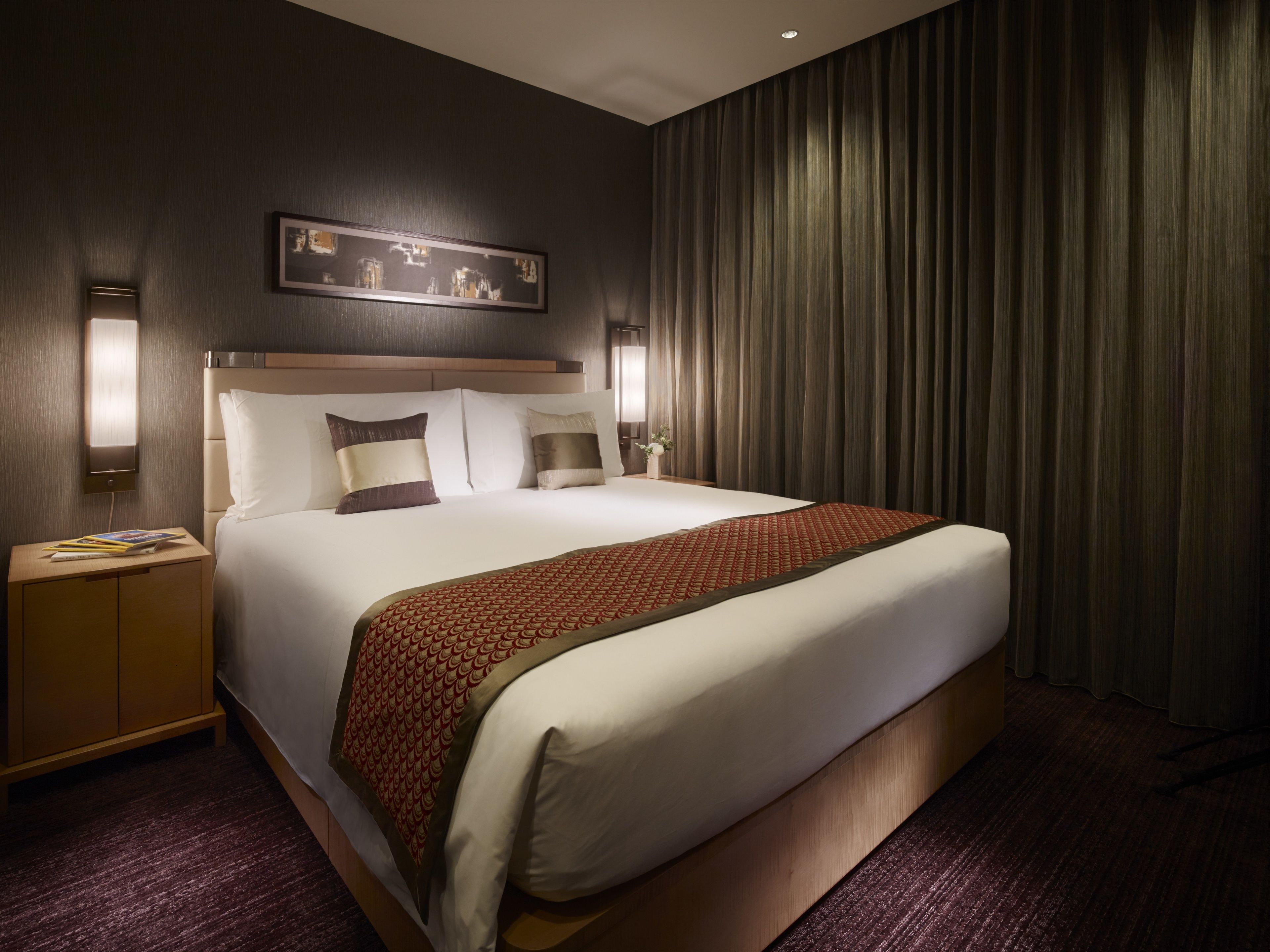 A hotel room with a large bed, a nightstand, a wall-mounted light, and a curtain.