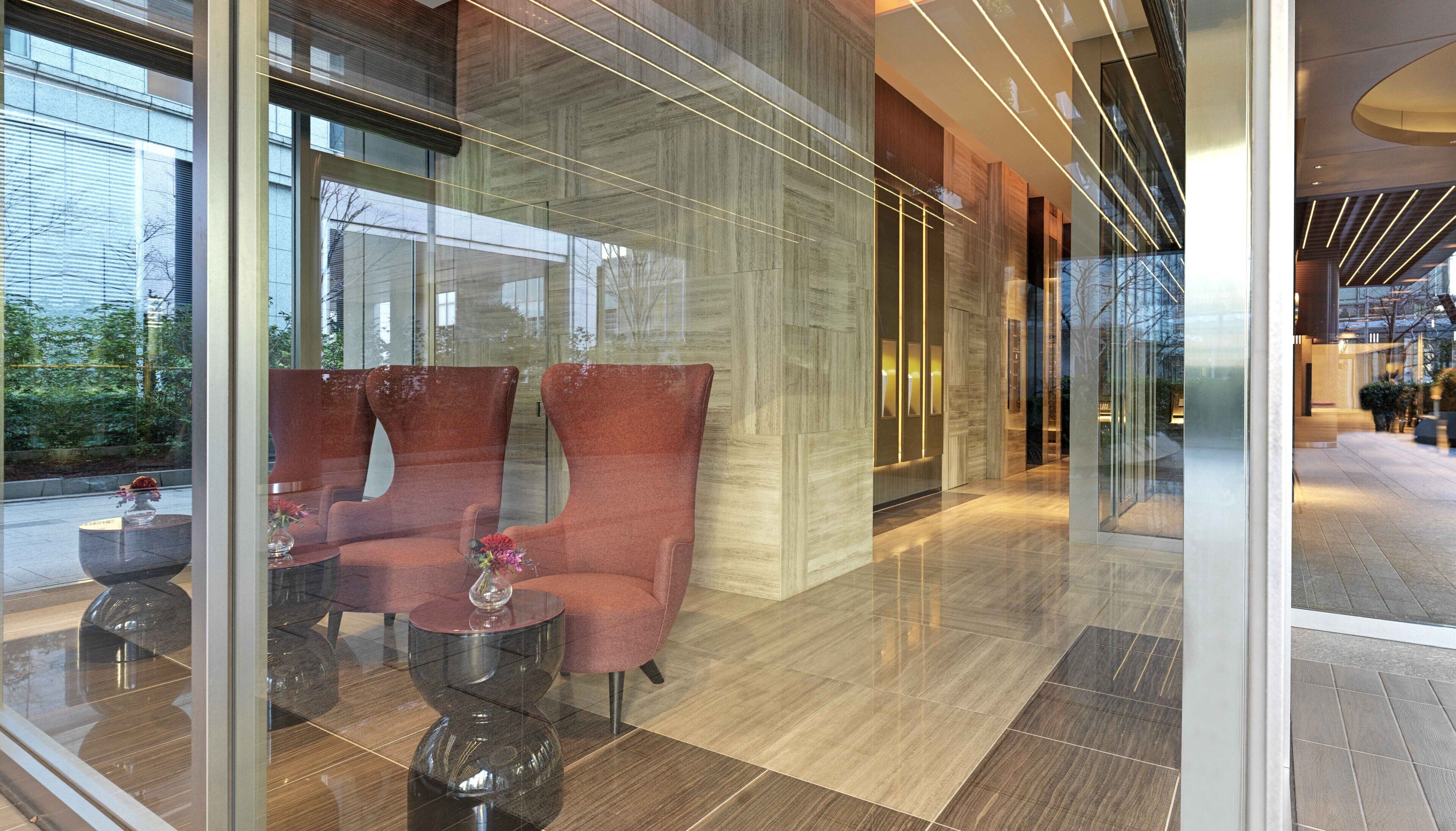 A modern lobby with a glass partition, two plush armchairs, a small table with a vase, and a polished floor.