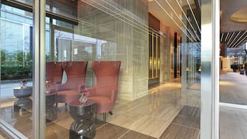 Un hall d’entrée moderne avec une cloison en verre, deux fauteuils confortables, une petite table avec un vase et un sol ciré.