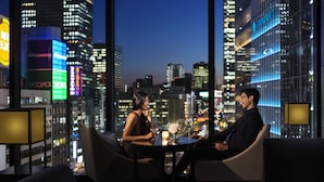 Una pareja sentada en una mesa con vista a la ciudad, mobiliario moderno e iluminación ambiental.