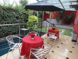 A patio area with a round table and chairs, a black umbrella, and a small pool. - Redsquare Home (Pretoria)