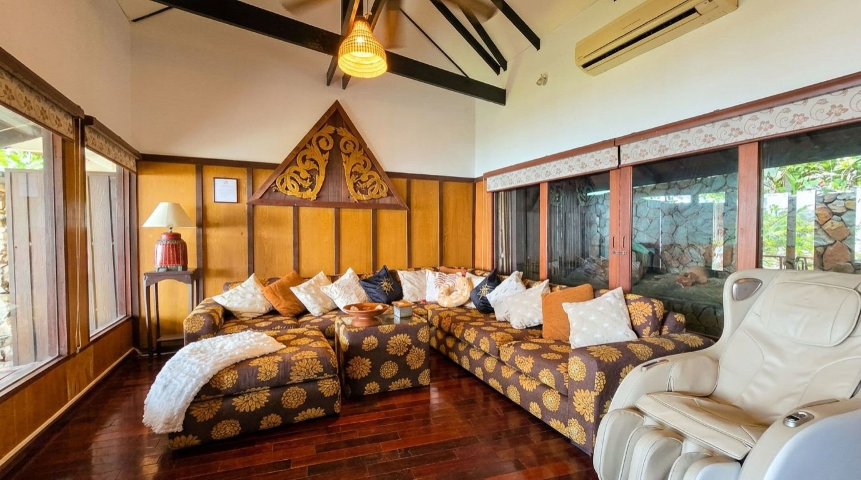 A room with a large sectional sofa, a white armchair, a lamp, and a decorative wall piece.