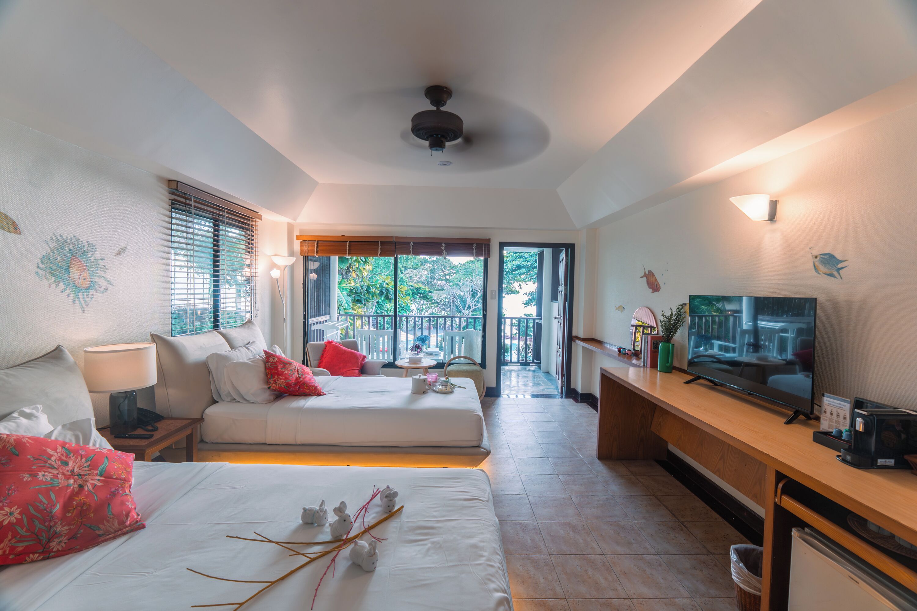 Habitación de hotel con dos camas, televisión, escritorio y balcón con vistas.