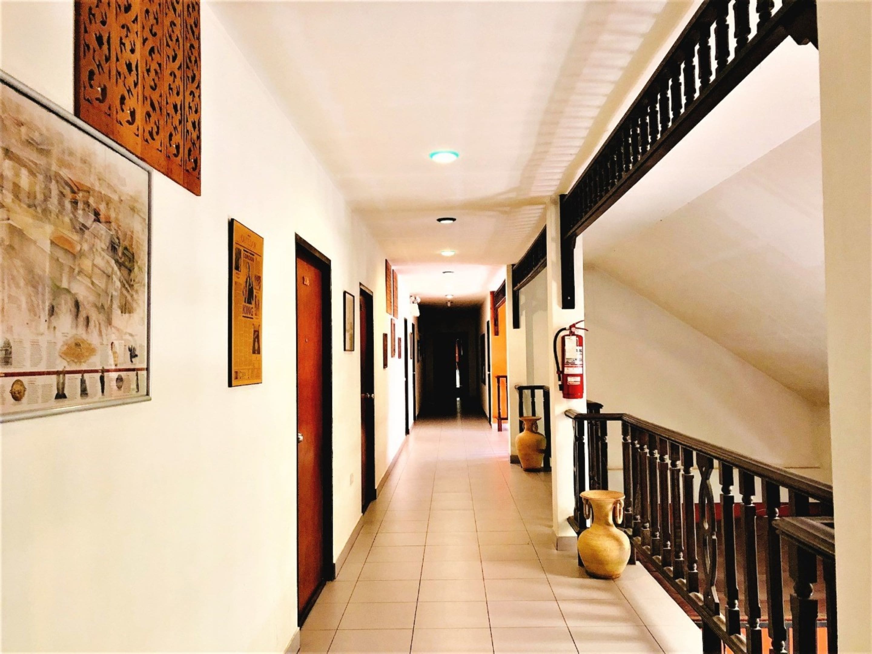 A hotel hallway with a tiled floor, wooden doors, and a staircase with a black railing.