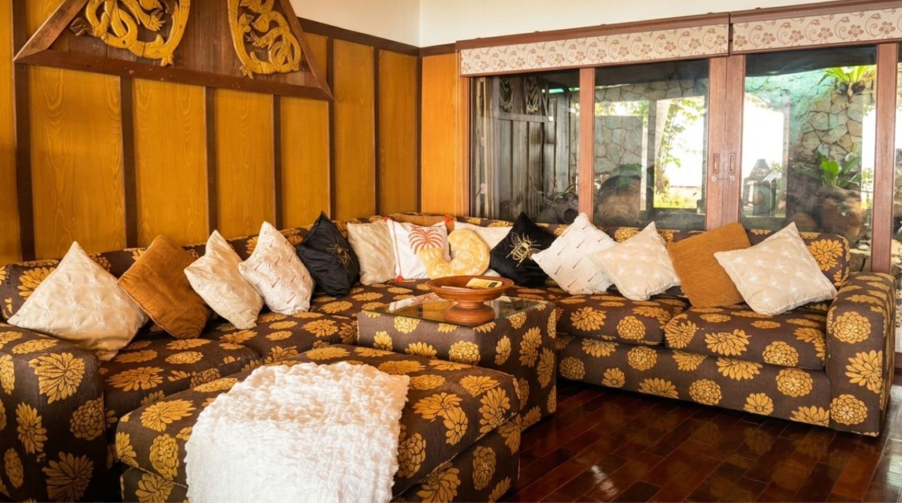 A room with a sofa set, pillows, a bowl, and a wooden headboard.