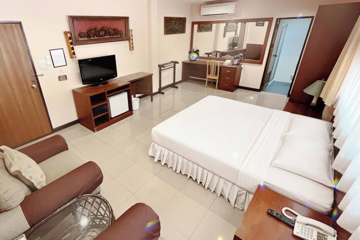 A hotel room with a bed, a sofa, a TV, a desk, a chair, and a bathroom mirror.