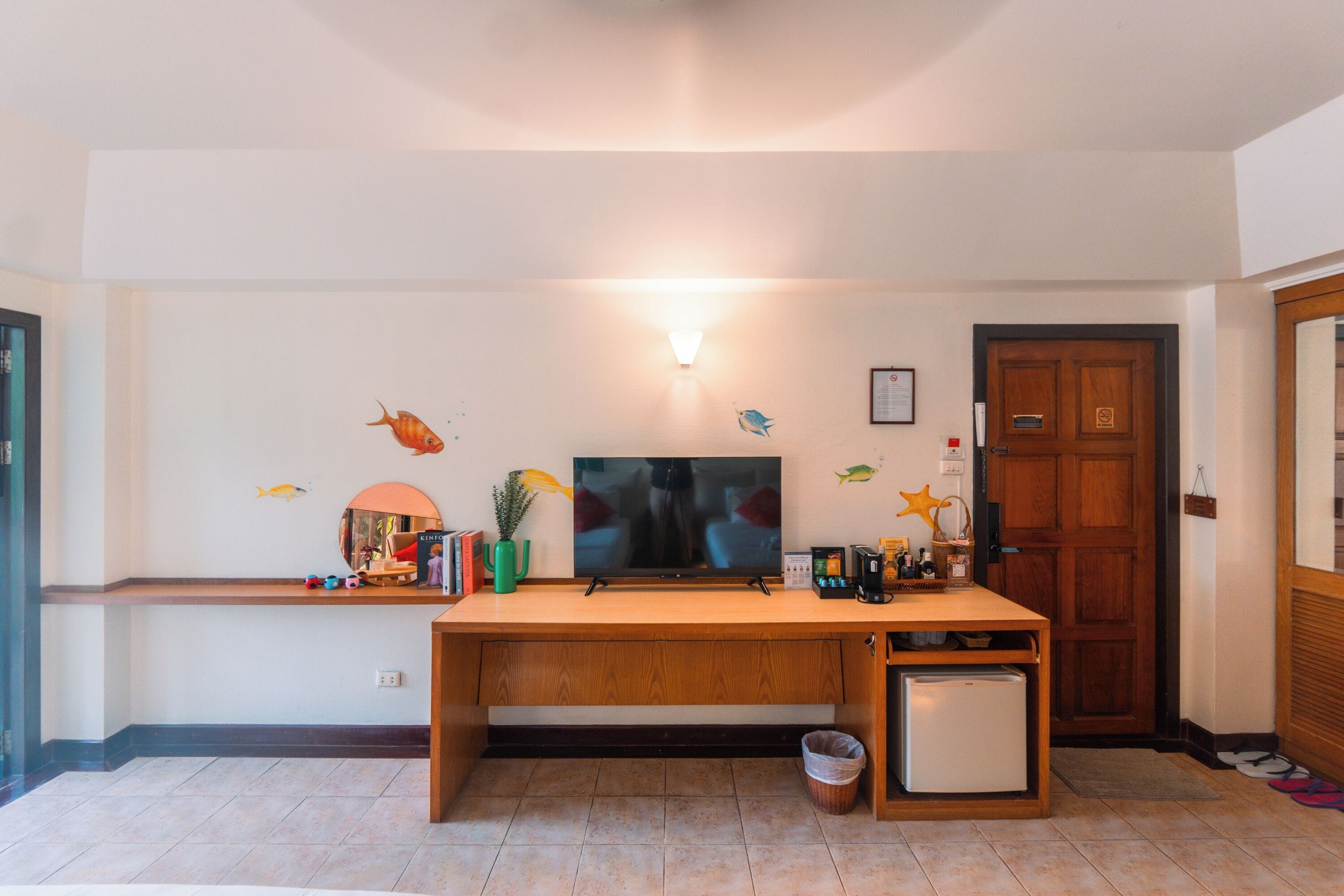 A living room with a wooden desk, a television, a small refrigerator, and decorative wall stickers.