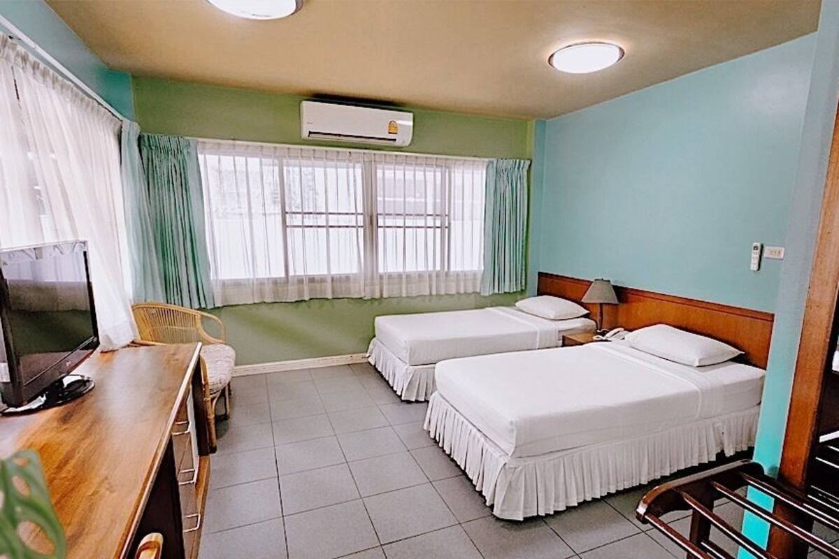 A hotel room with two beds, a desk with a computer, a chair, and an air conditioning unit.