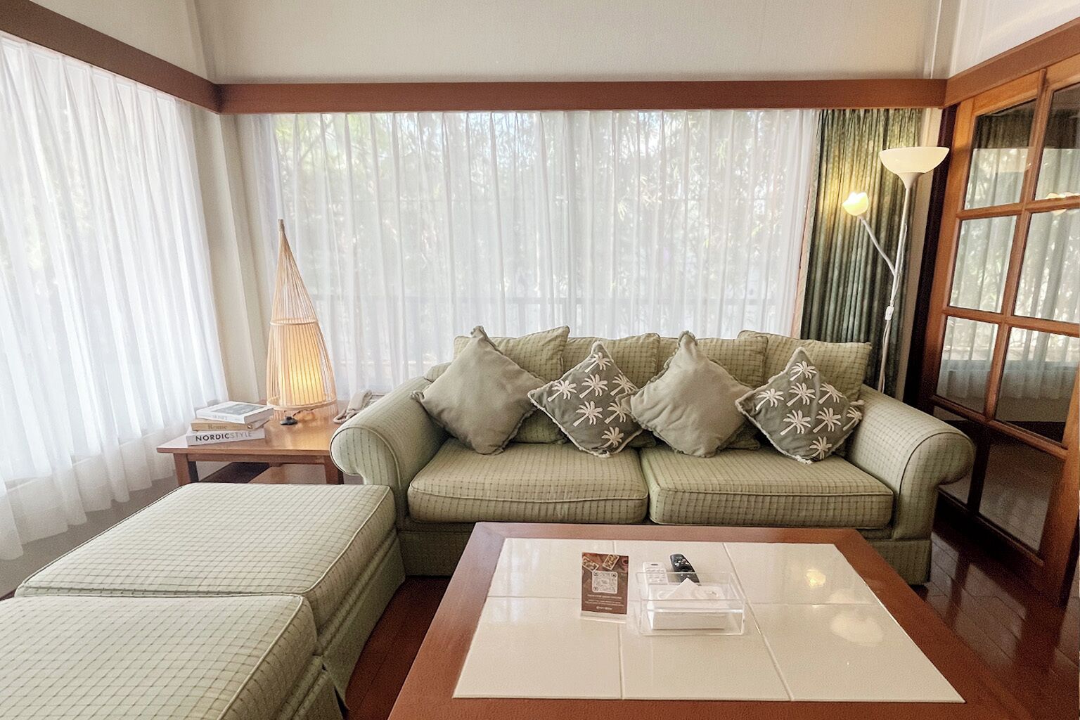A living room with a sofa, a coffee table, a lamp, and a window with curtains.