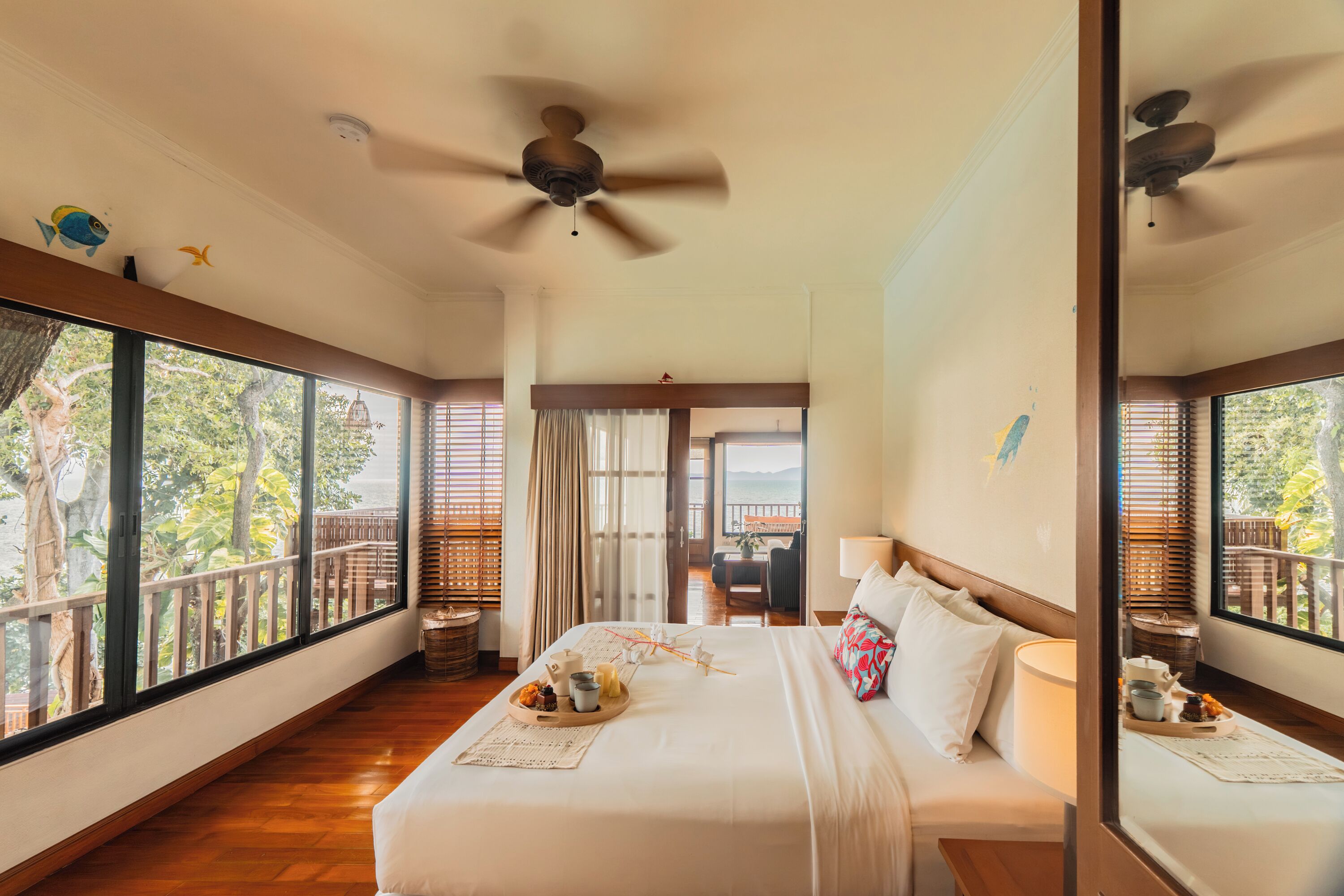 Un dormitorio amplio con una cama grande, un ventilador de techo y vistas al exterior a través de amplios ventanales.