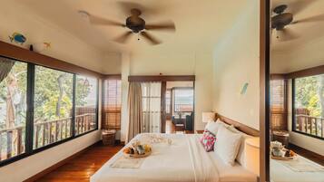Un dormitorio amplio con una cama grande, un ventilador de techo y vistas al exterior a través de amplios ventanales.