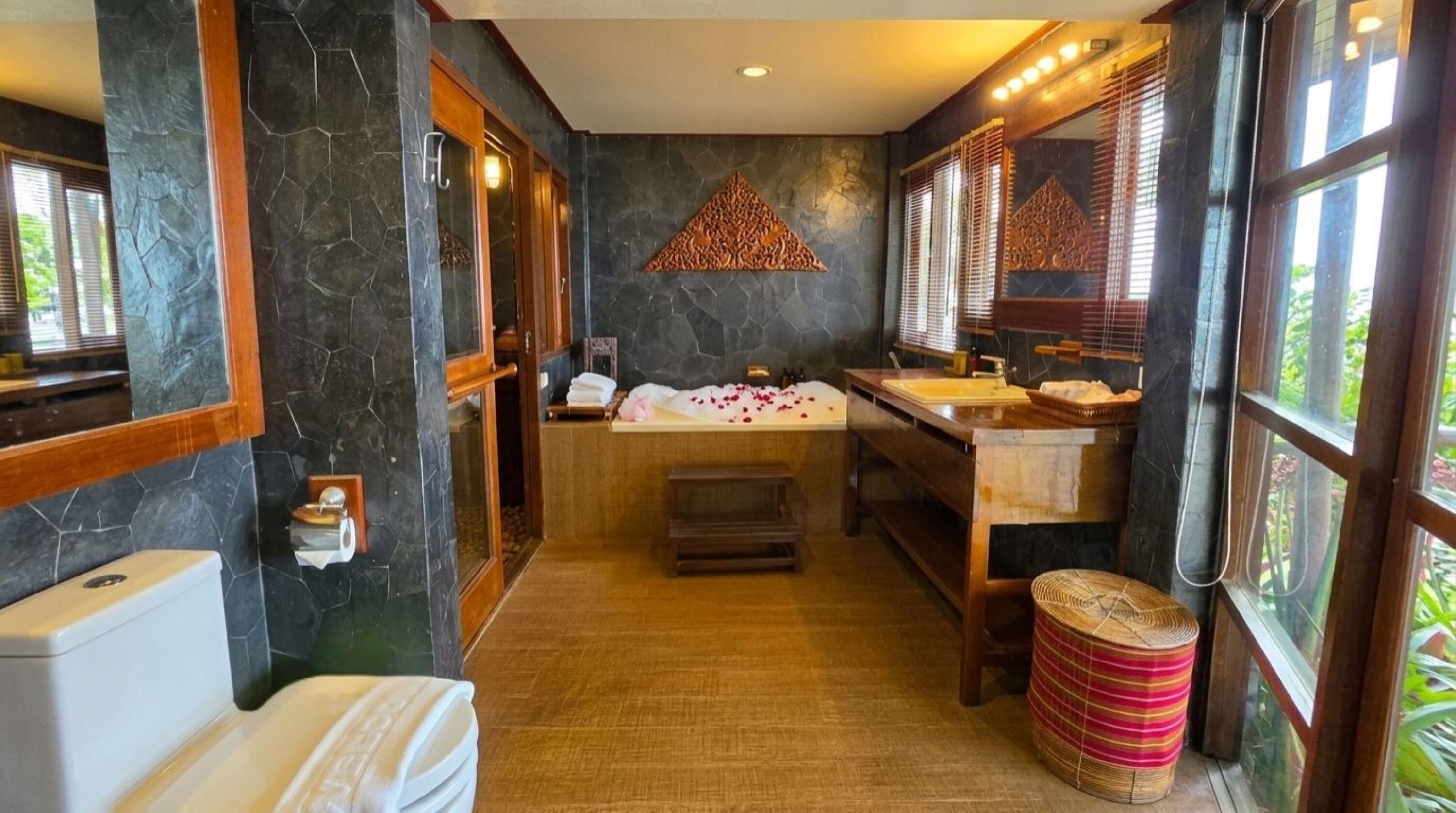 A bathroom with a stone wall, a wooden bench, a sink, and a toilet.