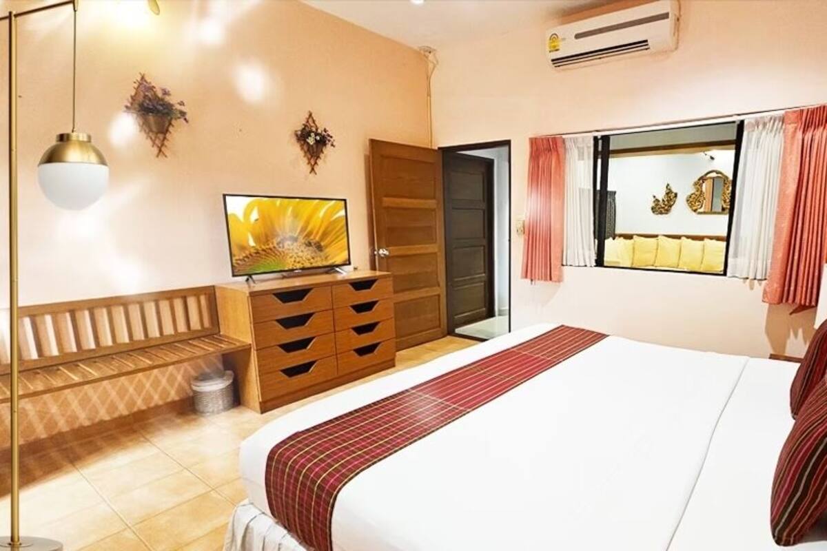 A bedroom with a bed, a TV, a dresser, a bench, a window with curtains, and wall decorations.
