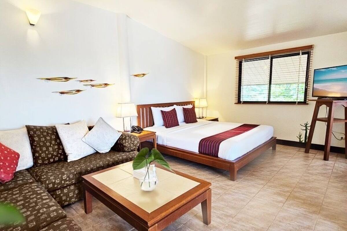 A hotel room with a sofa, two beds, a TV, and a plant.