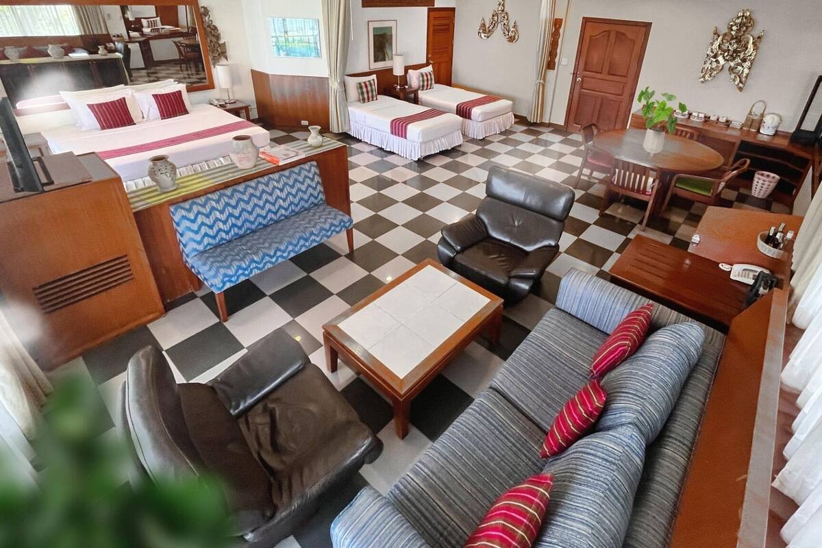 A hotel room with a checkered floor, a sofa, a dining table, a chair, and a bed.
