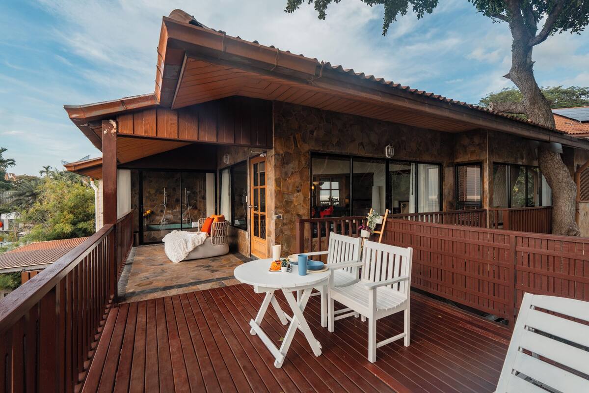 A wooden deck with outdoor seating and a stone building with a tiled roof.