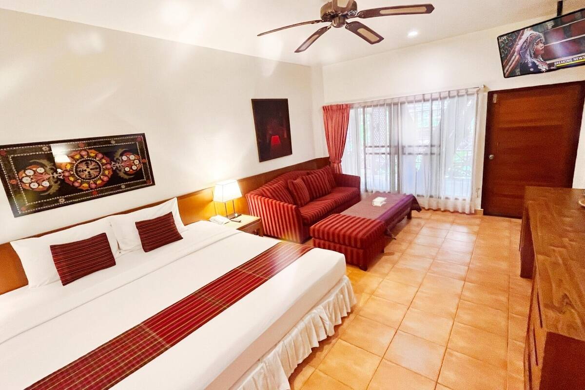 A hotel room with a bed, a sofa, a TV, and a ceiling fan.