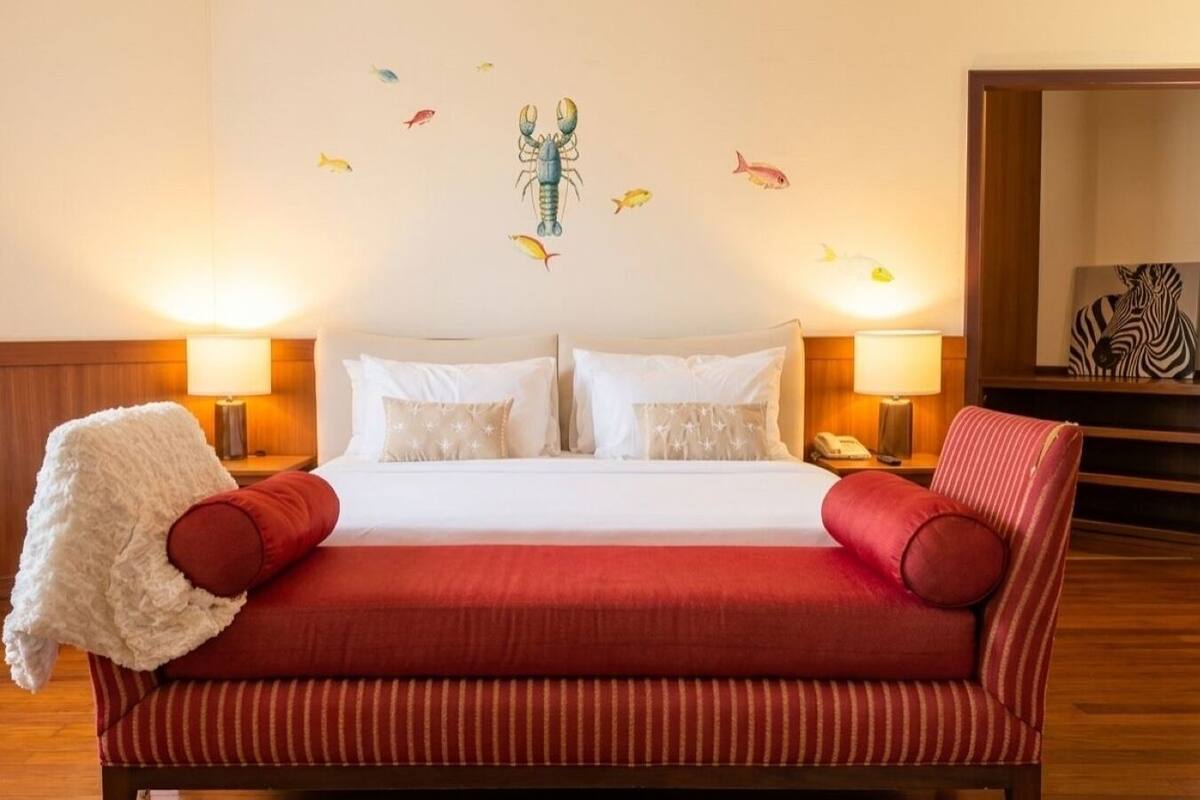 A hotel room with a large bed, two bedside lamps, a red-striped sofa, and a wall with fish decals.
