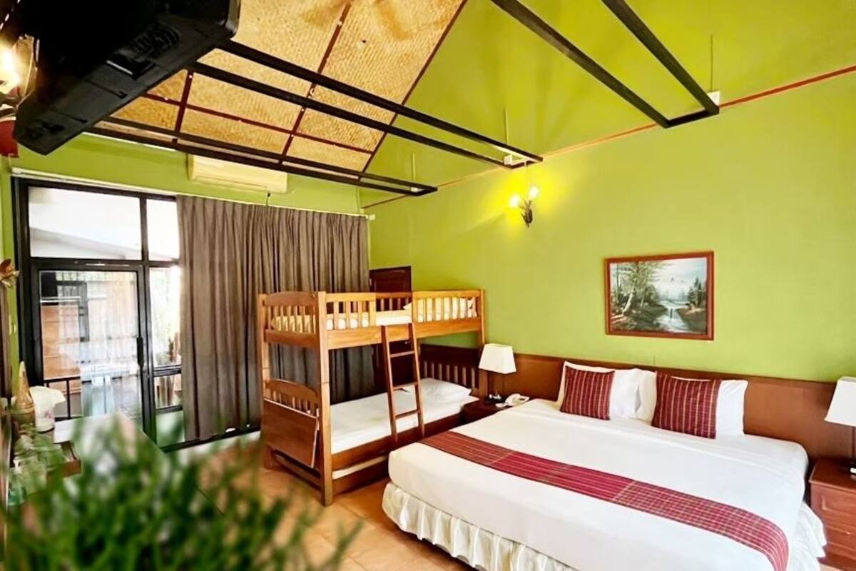 A room with a bunk bed, a large bed, a window with curtains, a painting on the wall, and a plant in the corner.