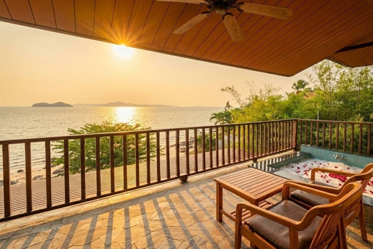 A balcony with a wooden table and chairs, a bathtub with rose petals, and a view of the sea and distant islands.