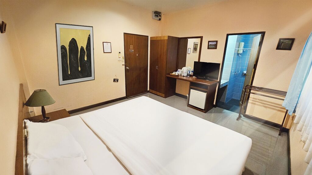 A hotel room with a bed, a desk with a television, a mirror, and a shower area.