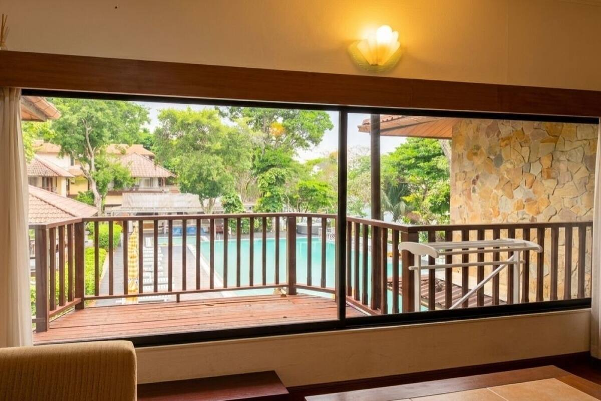 A room with a view of a swimming pool, a wooden deck, and a stone wall.