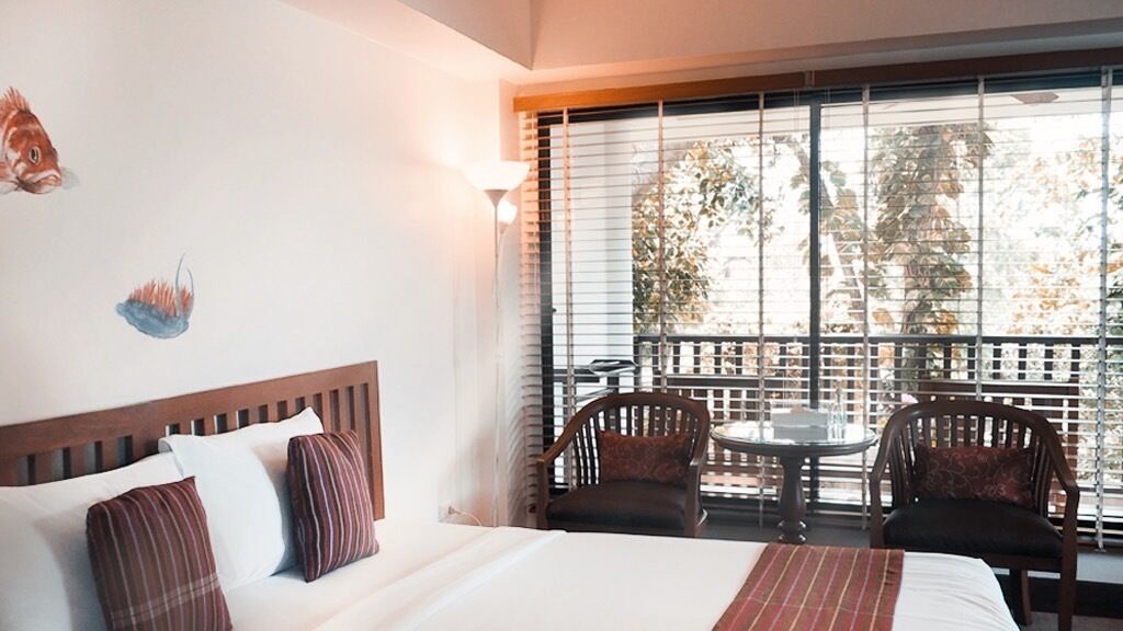 A hotel room with a bed, two chairs, a small table, and a balcony with a railing.
