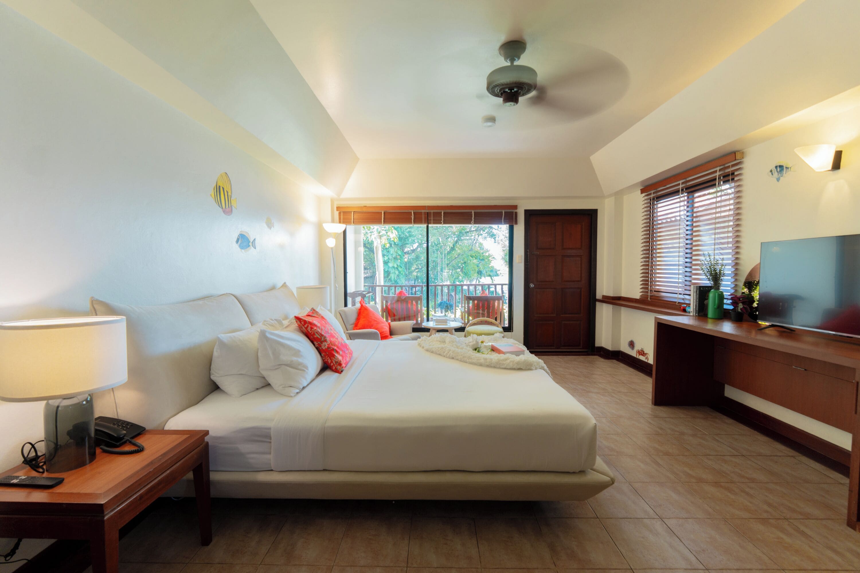 A hotel room with a bed, bedside table, lamp, TV, and a view of the outdoors.