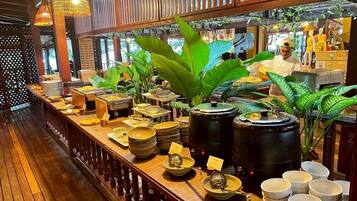 Una mesa de buffet con diversos platos y utensilios, un dispensador grande de agua negra, y plantas en macetas.