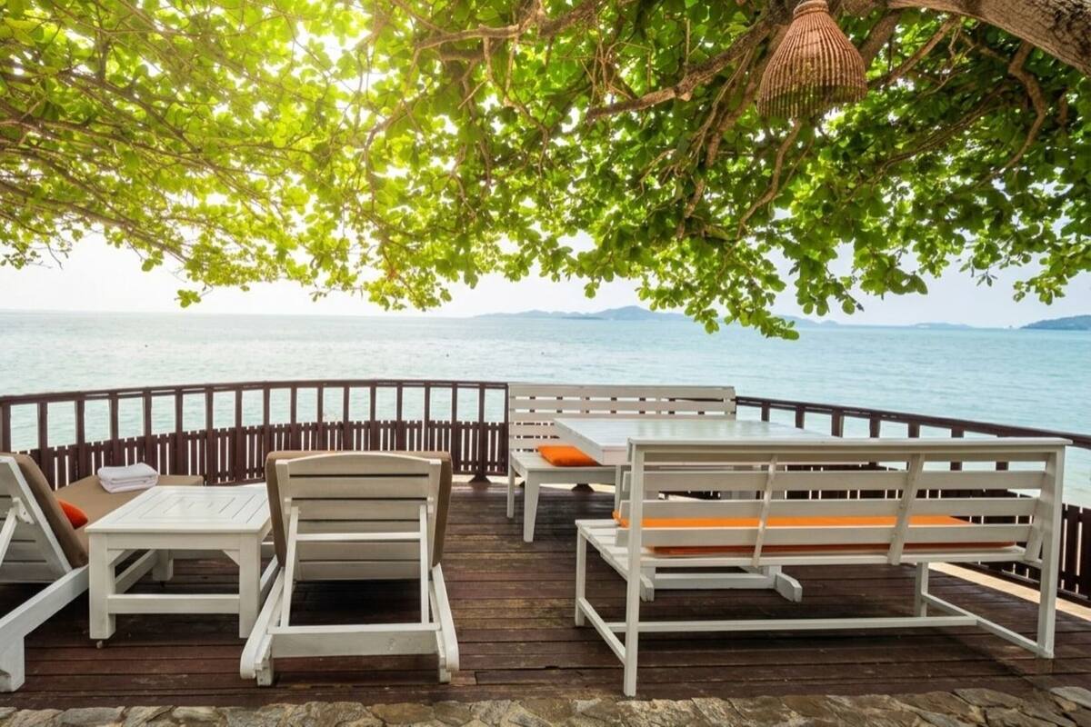 A wooden deck with white furniture and a view of the sea.