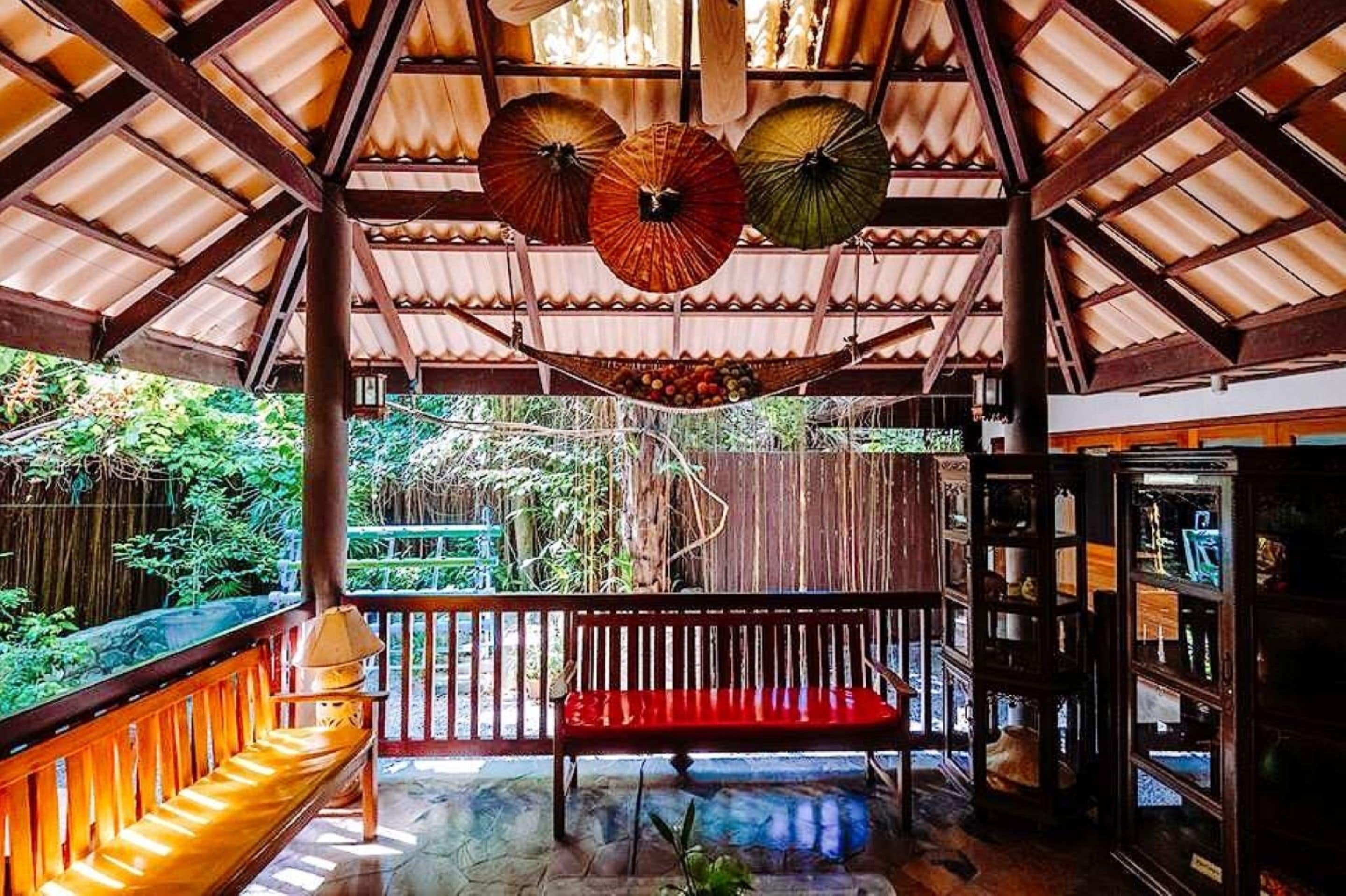 A covered outdoor area with a wooden bench, hanging umbrellas, and a wooden structure with glass display cases.