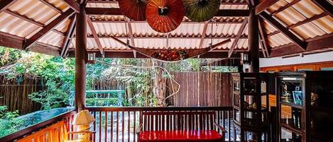 A covered outdoor area with a wooden bench, hanging umbrellas, and a wooden structure with glass display cases.