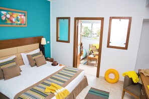 A hotel room with a large bed, a wooden headboard, a nightstand with a lamp, a colorful artwork on the wall, and a view of the outside balcony. - AQI Skanes Resort (Monastir)