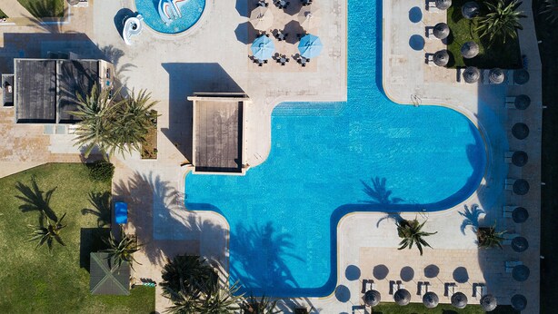 An aerial view of a resort with a large swimming pool, sun loungers, and palm trees. - AQI Skanes Resort (Monastir)