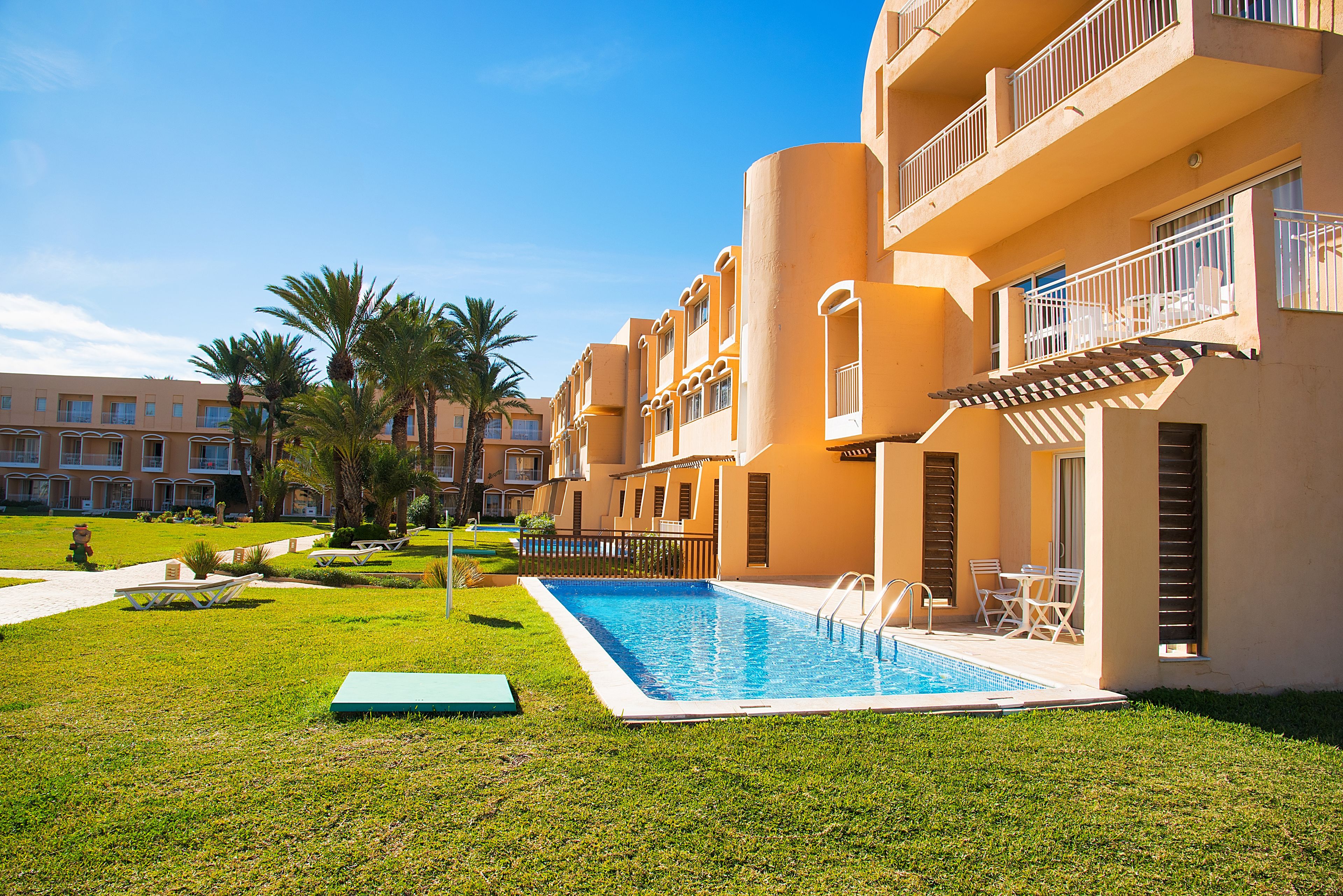 Un hotel con piscina, mobiliario exterior y palmeras.