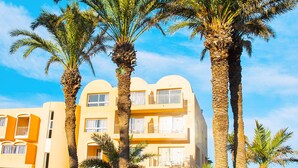 A hotel with multiple floors, balconies, and a well-maintained garden with palm trees. - AQI Skanes Resort (Monastir)