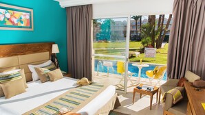 A hotel room with a large bed, a desk, a chair, and a view of a pool and outdoor area. - AQI Skanes Resort (Monastir)