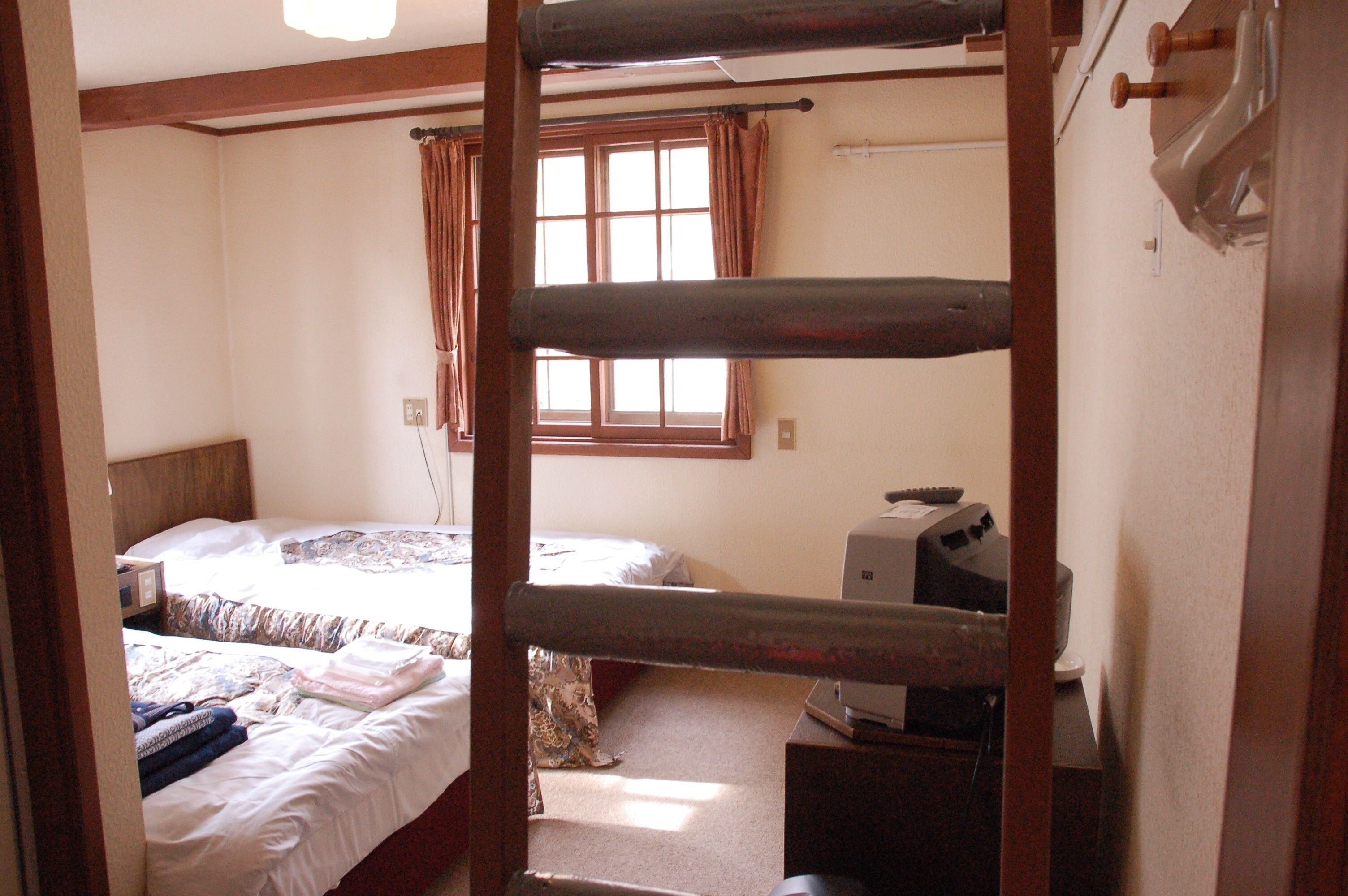 A room with bunk beds, a window with curtains, a desk with a computer, and a wall-mounted heater.