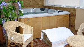 A spa room with a hot tub, wicker chairs, and a table. - Casa Aurelia (Palermo)