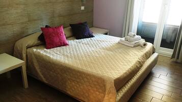 A hotel room with a large bed, a bedside table, a window with blinds, and a wooden floor.