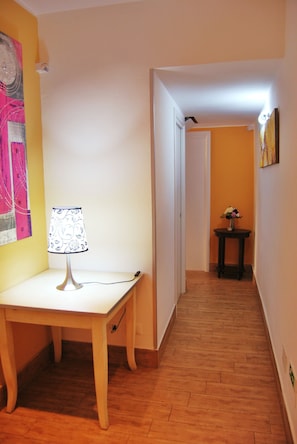 Un couloir avec une lampe sur une table, une porte au fond et une petite table ornée de fleurs.